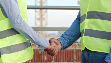 Close-up-of-the-African-American-male-hand-and-Caucasian-female-hand-shaking-at-the-building-site.-Builder-greeting-with-architect.